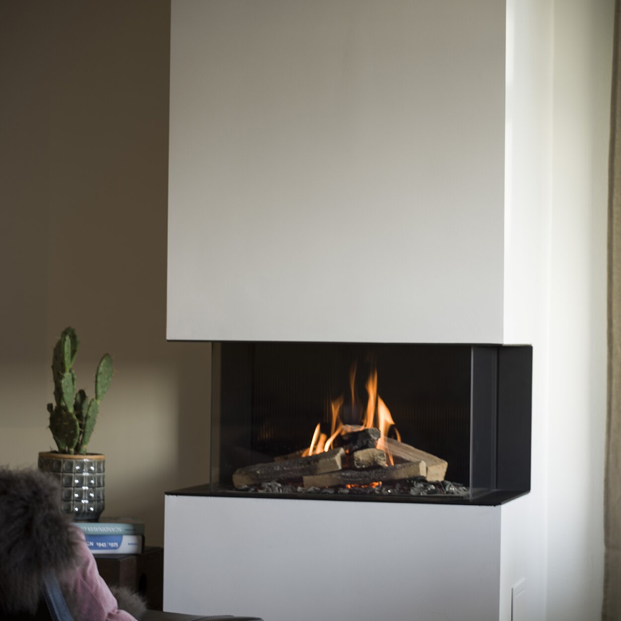 VISIO 90 3S gas fireplace as a 3-sided fireplace with a quiet gas flame in a white cladding next to a plant and reading chair