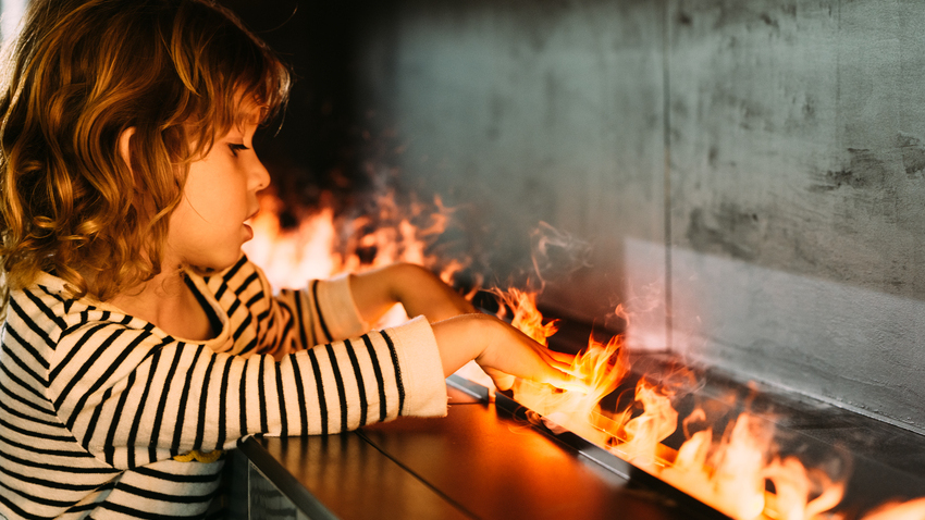 Un enfant met ses mains dans les flammes de vapeur d'eau froide du feu électrique Cassette 1000 de Dimplex.