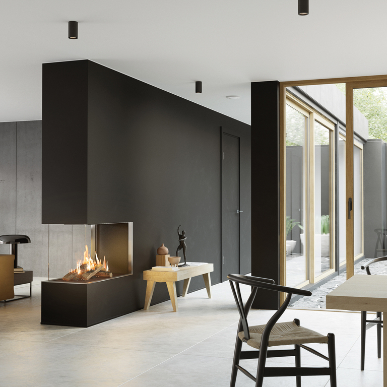 La cheminée à gaz VISIO 90 RD s'intègre idéalement comme séparateur de pièce dans un mur noir entre le salon et la salle à manger et structure l'espace de vie à la décoration sobre
