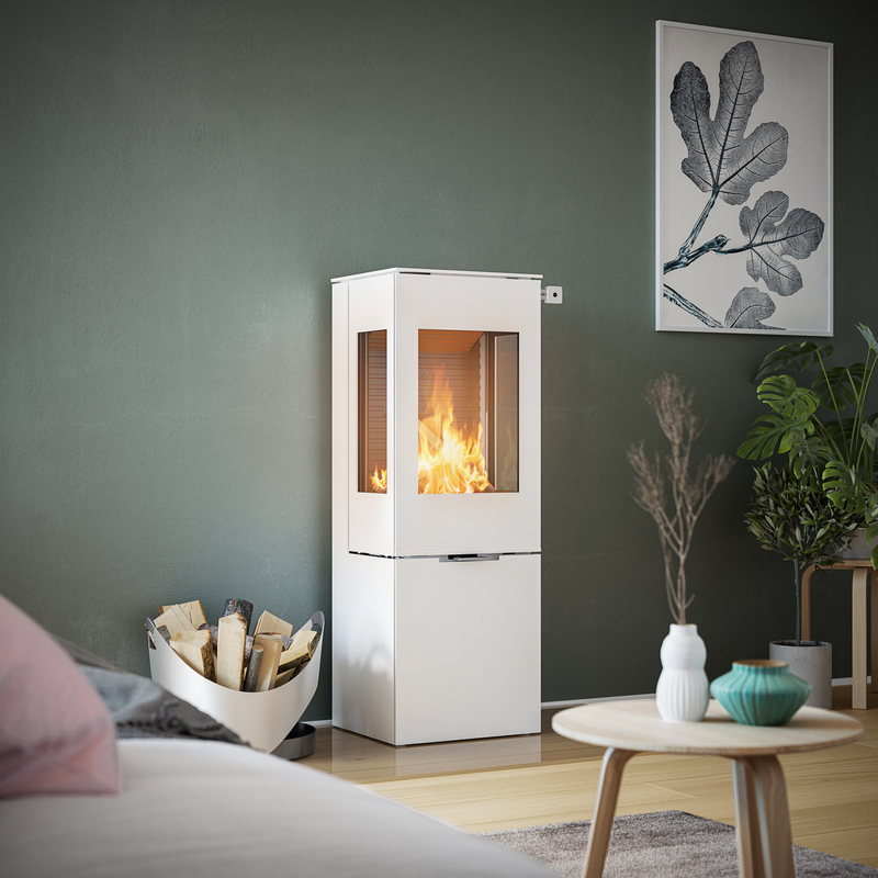 Wood stove NEXO 120 in white with steel door and two side windows in front of a green wall in a decorative living area