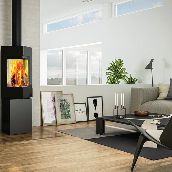 Holz-Kaminofen Q-BE in Schwarz mit Stahltür mit grossem Feuer in moderner Wohnung auf dem Land