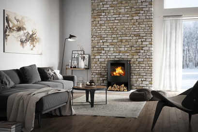 Wood stove Q-TEE 2 C in black with wood compartment in its slightly oval shape as fireplaces in a rustic country house