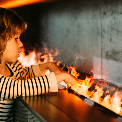 Ein Kind hält seine Hände in die kalten Wasserdampf Flammen des Elektrofeuer Cassette 1000 von Dimplex