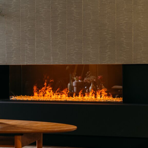 Elektrokamin eMatriX Linear 1300/400 zweiseitig verglast im gemütlichen Wohnzimmer mit Holztisch und Blumen-Dekoration