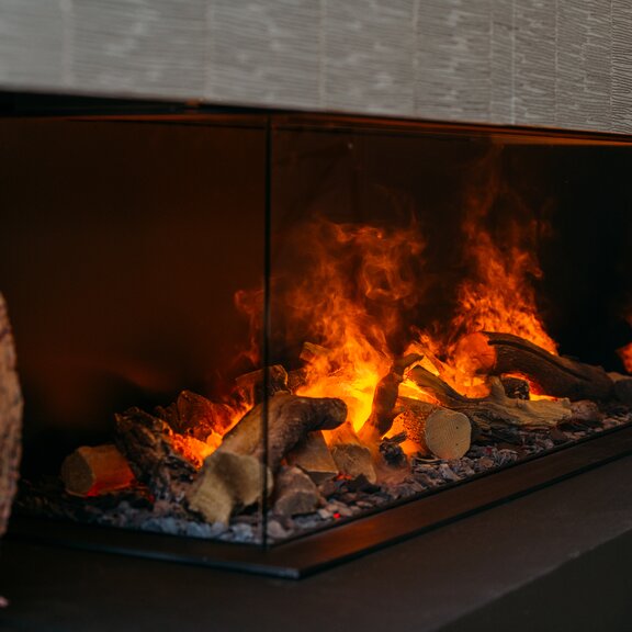 Electric fireplace e-Matrix Linear 1300/400 3-sided glazed by Dimplex installed on a dark stone wall with cushions as decoration