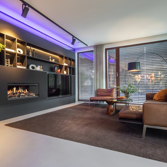 The electric fireplace E-One 100 Front is integrated into black living room furniture with LED lighting.