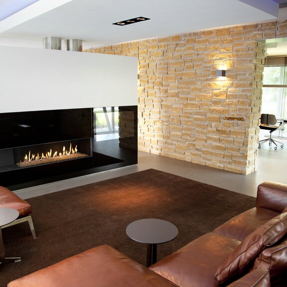 Gas-Kamin G125/37C eingebaut in eine Trennwand im Wohnzimmer mit Steinwänden und Ledermöbel