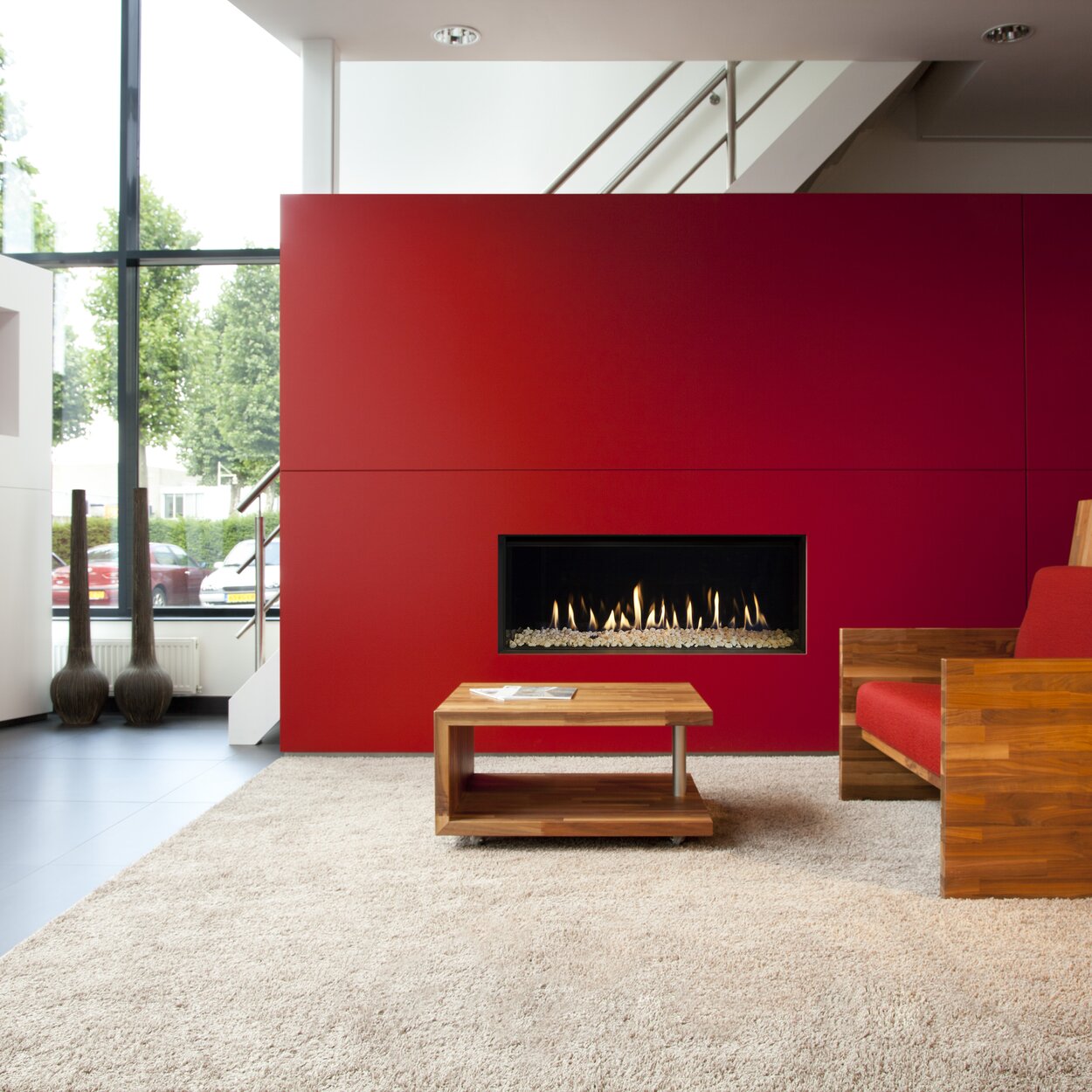 Cheminée à gaz G100/41F de Kalfire avec des pierres blanches dans la chambre de combustion dans un appartement avec des murs en rouge et blanc et des meubles en bois
