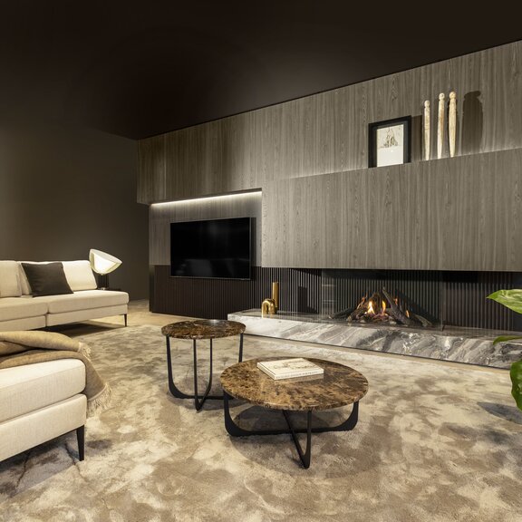Camino a gas Gi115/55S con rivestimento in legno e pietra nel soggiorno, con divano bianco, cuscini e coperte e tappeto beige