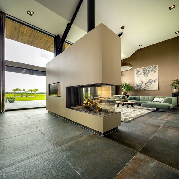 Room divider gas fireplace GP115/75R with sand-coloured cladding in the living room with large window fronts and a view of the green landscape