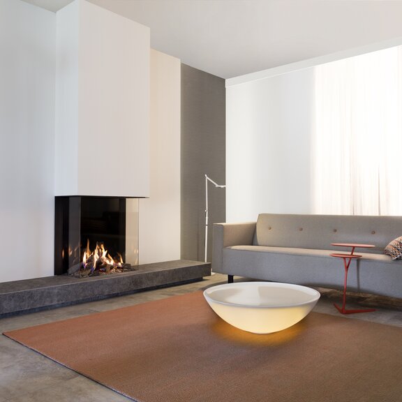 Gas-Kamin GP70/75S dreiseitig verglast auf Steinaufsatz an weisser Wand im schlichten und modernen Wohnzimmer