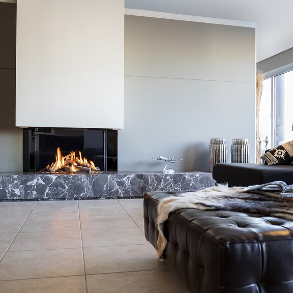 Gas-Kamin GP85/55S dreiseitig verglast mit beiger Verkleidung im gemütlichen Wohnzimmer mit Sofa
