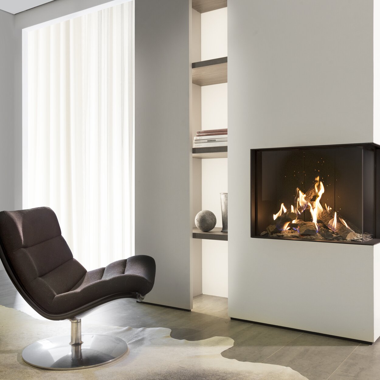 Version d'angle de la cheminée à gaz GP65/55C avec habillage blanc dans un salon sobre et lumineux avec fauteuil