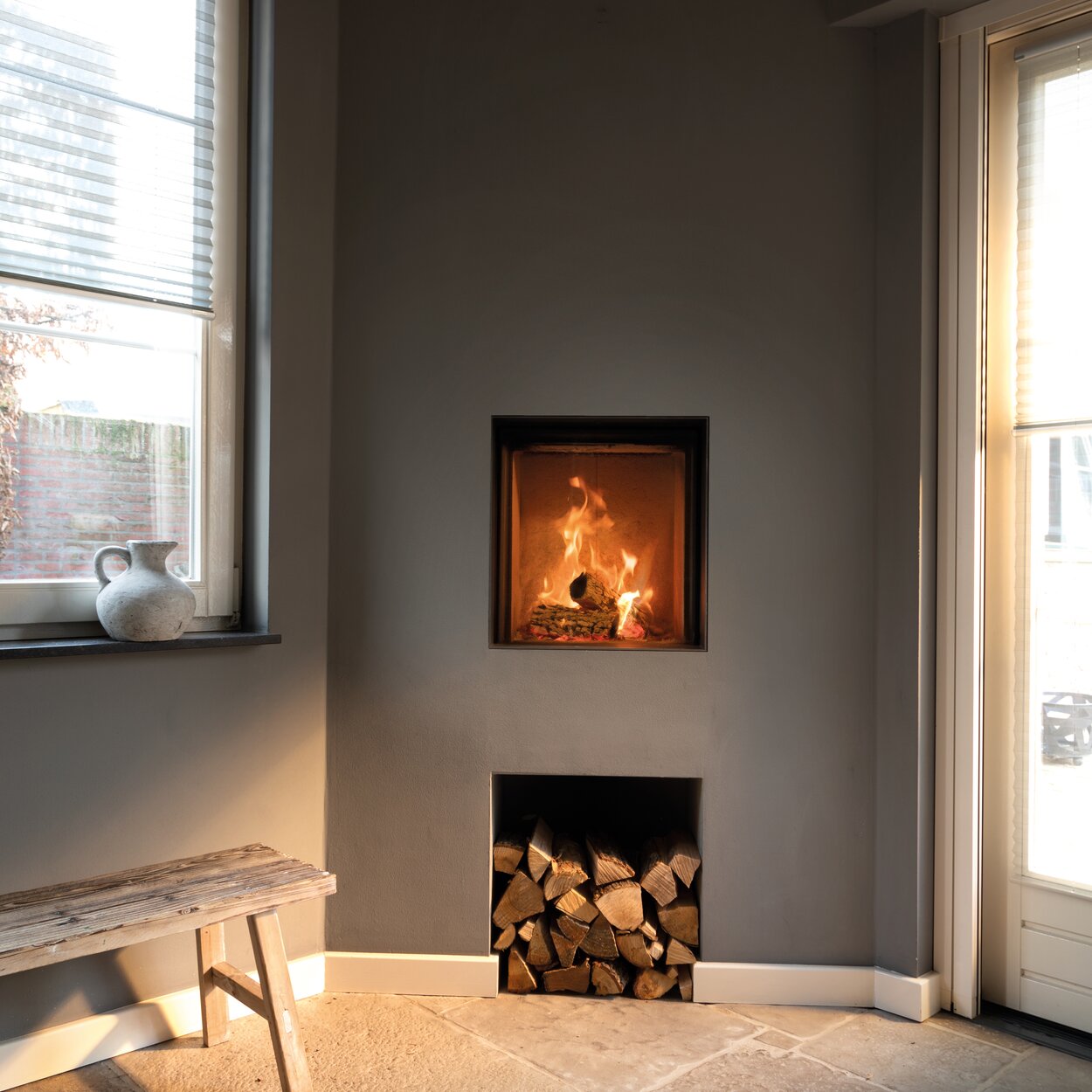 Wood fireplace W45/48F by Kalfire in front version as a compact fireplace in a grey wall with practical compartment for wood logs