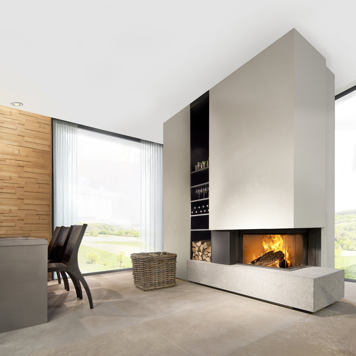 Wood fireplace W65/38C by Kalfire. The 2-sided fireplace (right) is built into a beige-coloured partition wall and stands on a modern bench made of natural stone