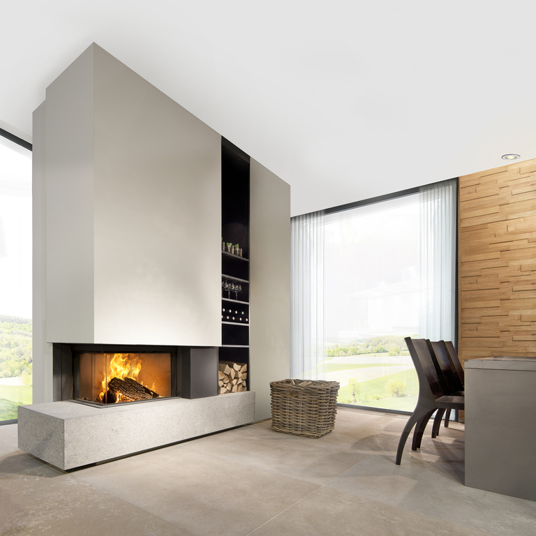 Wood fireplace W65/38C by Kalfire. The 2-sided fireplace (left) is built into a beige-coloured partition wall and stands on a modern bench made of natural stone