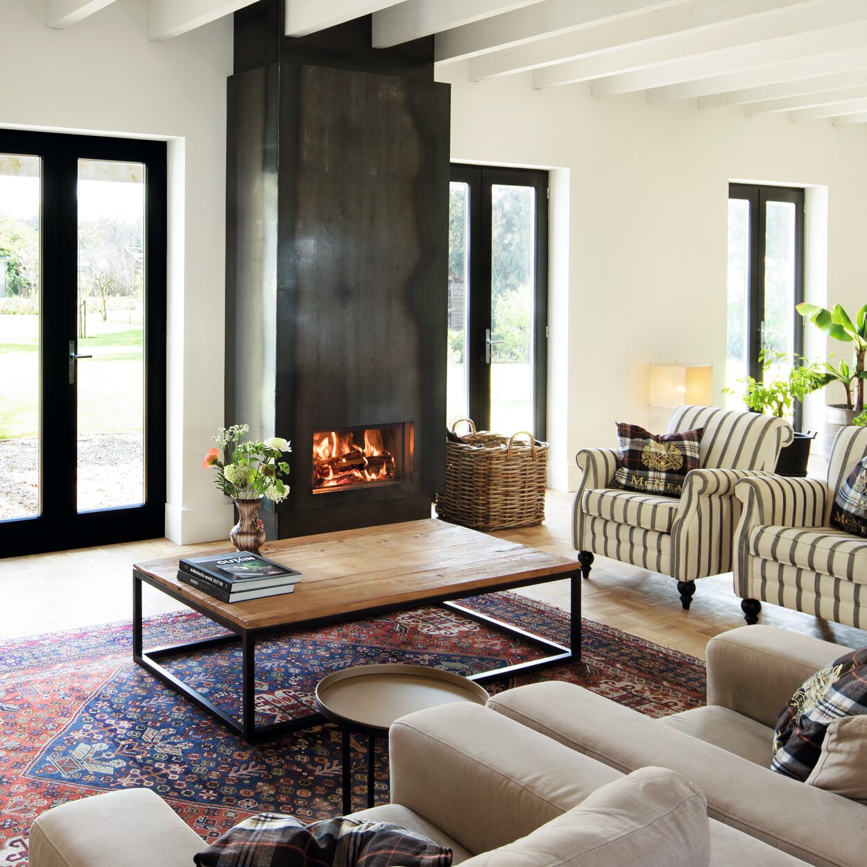 Wood fireplace W70/33F by Kalfire in a large, bright living room with black steel cladding and classic armchairs