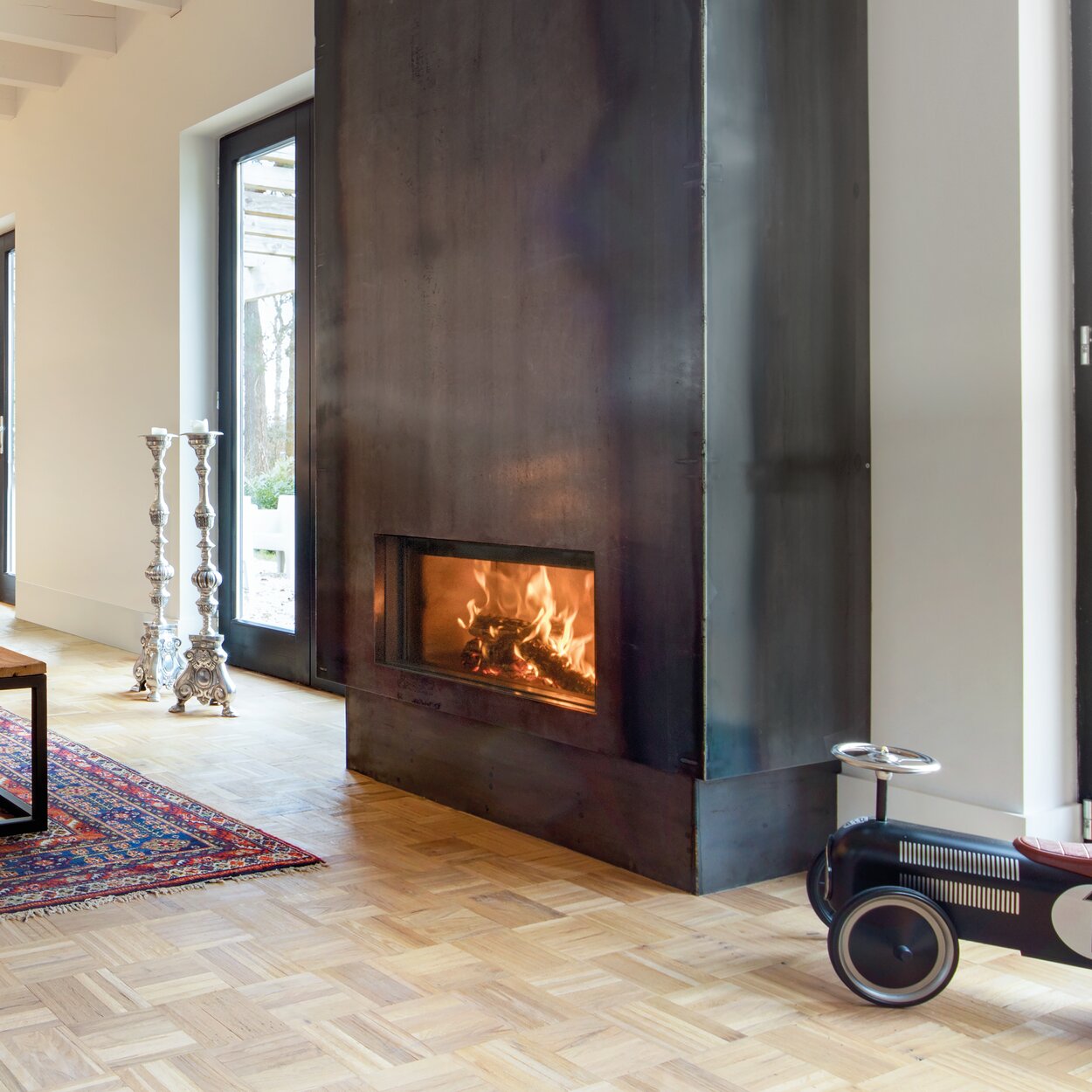  Holz-Kamin W70/33F von Kalfire in grossem, hellen Wohnraum mit schwarzer Stahlverkleidung neben einem Spielzeugauto