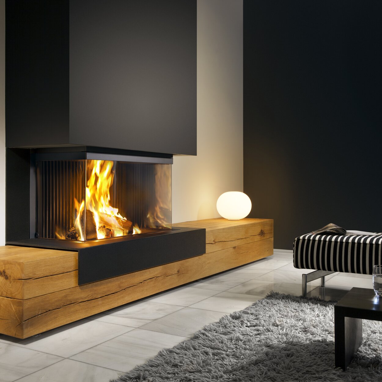 Wood fireplace W90/47S 3-sided by Kalfire stands on a wooden bench in a modern living room