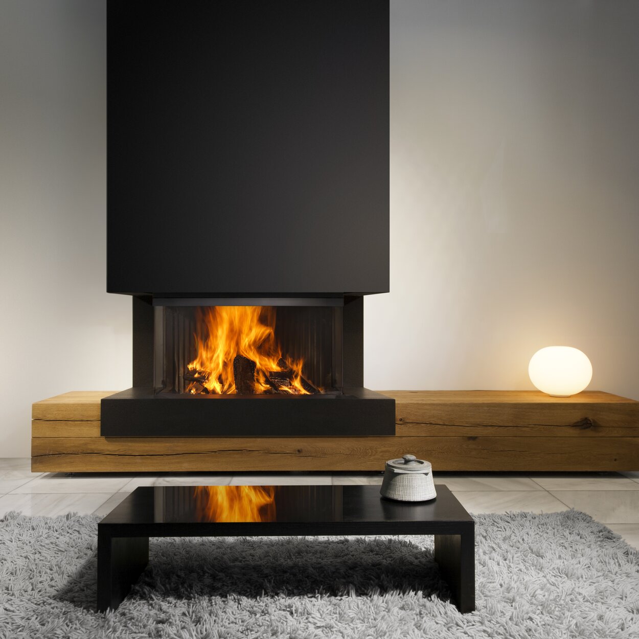 Wood fireplace W90/47S 3-sided by Kalfire stands on a wooden bench in a modern living room